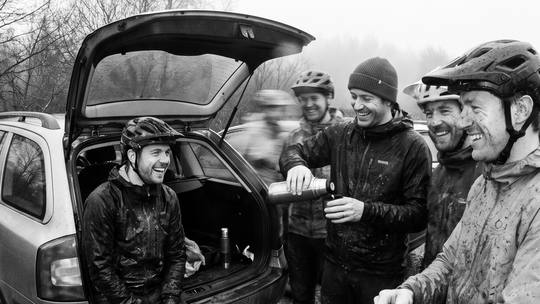 riders round an open car boot at the trailhead, pouring tea from a flask