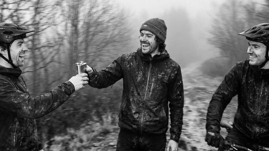 riders sharing a hip flask on a muddy trail, bikes beside them