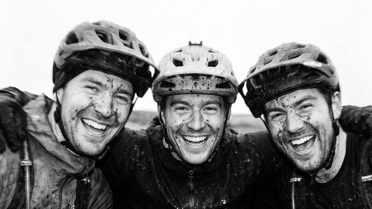 three mud-splattered riders, arms round each other, grinning at the camera