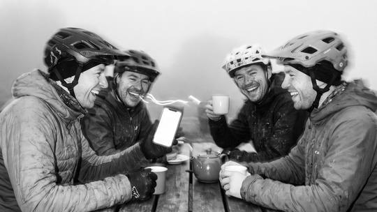 riders leaning in over a phone at a café table
