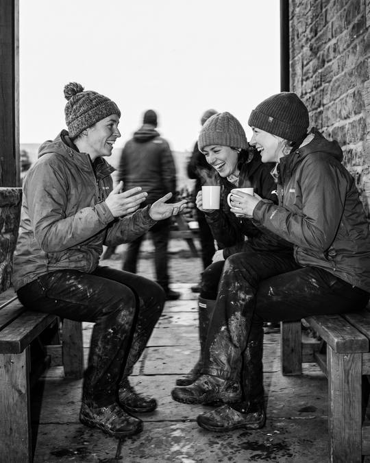 three riders in beanies with mugs of tea on a stone porch bench, the ride done