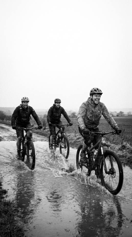 three riders laughing as they splash through a big puddle